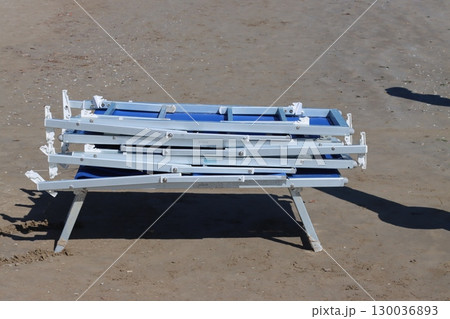Stack of folded beach chairs sitting on sandy beach 130036893