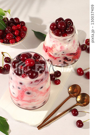 Fruit yogurt with cherries and fresh cow cream for healthy nutrition in a glass on an elegant table. Healthy breakfast with ingredients, kitchen background. Natural food and detox diet concept Fruit yogurt with cherries and fresh cow cream for healthy nutrition in a glass on an elegant table. Healthy breakfast with ingredients, kitchen background. Natural food and detox diet concept 130037409