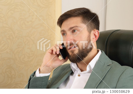 Businessman engaged in a phone call in a modern office setting during the day 130038629