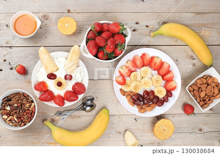 Useful breakfast of ingredients, strawberry yogurt with muesli, grapes, banana and honey on a bright table, fruit salad. Healthy and natural food concept, lifestyle, food for children, selective focus Useful breakfast of ingredients, strawberry yogurt with muesli, grapes, banana and honey on a bright table, fruit salad. Healthy and natural food concept, lifestyle, food for children, selective focus 130038684