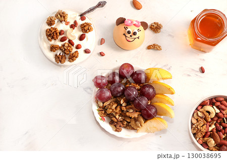 Healthy breakfast with ingredients, flat lay, fruit salad with muesli, apricots, grapes, honey and apple on a bright table. Healthy and natural food concept, lifestyle, top view, selective focus Healthy breakfast with ingredients, flat lay, fruit salad with muesli, apricots, grapes, honey and apple on a bright table. Healthy and natural food concept, lifestyle, top view, selective focus 130038695