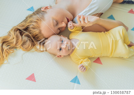 Mother and baby lying on a play mat. Tender bonding moment, cozy childhood atmosphere, and early development. Parenting, love, and infant care concept 130038787