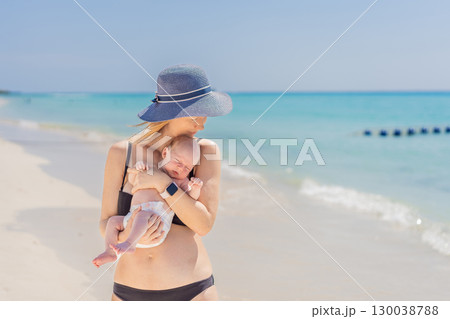 Mother holding her newborn baby by the turquoise sea, sharing a peaceful and loving moment. Family bonding, motherhood, and travel with baby concept Mother holding her newborn baby by the turquoise sea, sharing a peaceful and loving moment. Family bonding, motherhood, and travel with baby concept 130038788