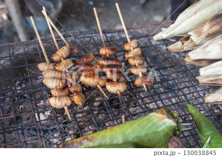 Grilled bamboo worms skewers cooking on outdoor charcoal grill with corn and banana leaves Grilled bamboo worms skewers cooking on outdoor charcoal grill with corn and banana leaves 130038845