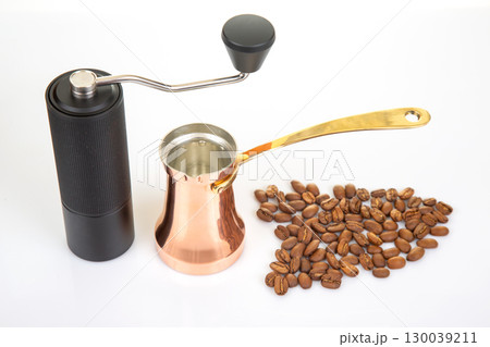 A black manual coffee grinder with a metallic handle sits beside a copper cezve  130039211