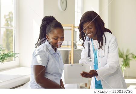Woman patient looking to report file with appointment sitting on couch in clinic with a doctor. Woman patient looking to report file with appointment sitting on couch in clinic with a doctor. 130039750