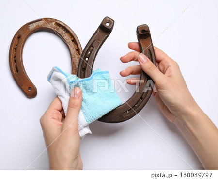 Hands Cleaning Rusty Horseshoe with Cloth on White Background Hands Cleaning Rusty Horseshoe with Cloth on White Background 130039797