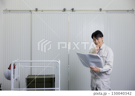倉庫で図面を見る作業着の男性 130040342