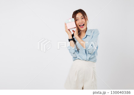 Gift sound mystery brings smile to the young Asian woman woman happy face as she listens excitedly to the pink box, unaware of another hidden gift meant just for her. isolated studio white background Gift sound mystery brings smile to the young Asian woman woman happy face as she listens excitedly to the pink box, unaware of another hidden gift meant just for her. isolated studio white background 130040386