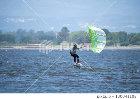 A middle-aged man in a wetsuit glides on a hydrofoil board with a green and white kite 130041108