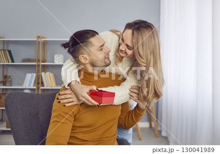 Happy woman holding red present box in her hand and congratulating her boyfriend on holiday. Happy woman holding red present box in her hand and congratulating her boyfriend on holiday. 130041989