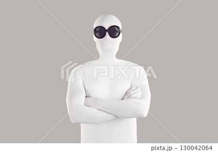 Portrait of man disguised in white bodysuit and black sunglasses standing with folded arms 130042064
