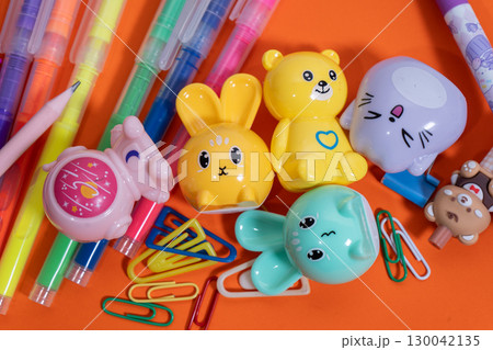 Colorful pencil sharpeners, pens, and paper clips lying on orange surface Colorful pencil sharpeners, pens, and paper clips lying on orange surface 130042135