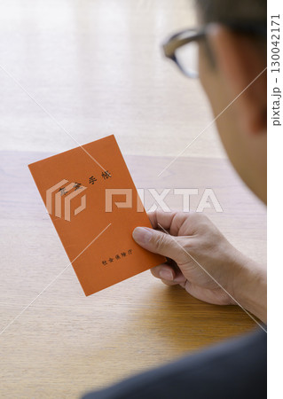 年金手帳を見つめる男性 130042171