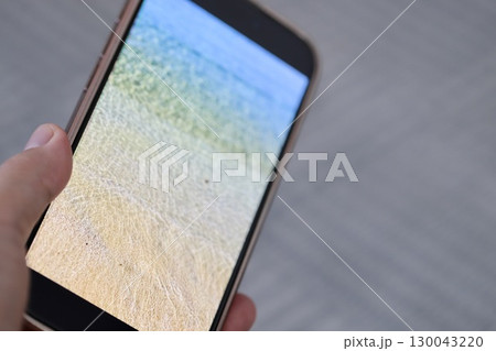 海の待ち受け画面のスマホを持つ手 130043220