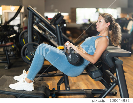 Sportive young girl training on hip thrust machine in gym 130044982
