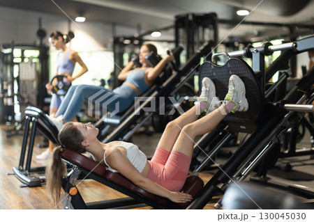 Sportive young girl training on leg press machine in gym Sportive young girl training on leg press machine in gym 130045030