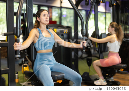 Sportive young girl training on chest fly machine in gym Sportive young girl training on chest fly machine in gym 130045058