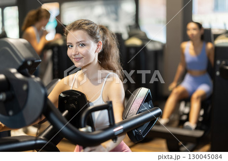 Positive young girl training on chest press machine in gym Positive young girl training on chest press machine in gym 130045084