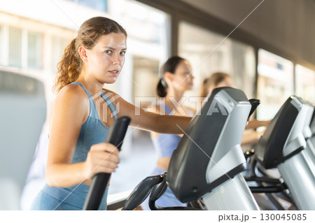 Sportive young girl training on elliptical machine in gym Sportive young girl training on elliptical machine in gym 130045085