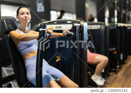 Sportive young girl training on chest press machine in gym Sportive young girl training on chest press machine in gym 130045142
