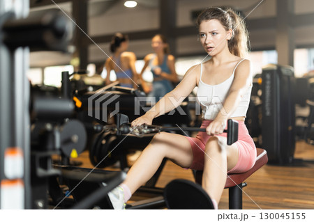 Sportive young girl training on cable row machine in gym Sportive young girl training on cable row machine in gym 130045155