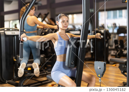 Sportive young girl training on chest fly machine in gym 130045182