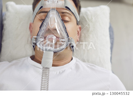 Portrait of a young man lying on a couch at home with an oxygen mask. Portrait of a young man lying on a couch at home with an oxygen mask. 130045532