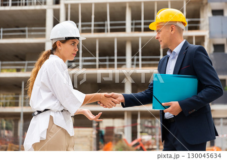 Man and woman in hardhats shaking hands in construction site 130045634