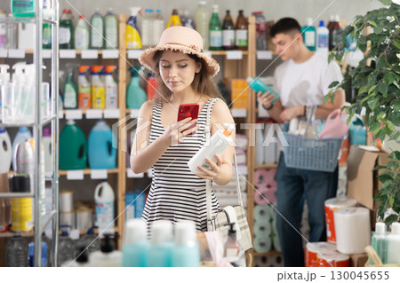 Girl buyer scans qr code on sunblock cream label, man shopping in background Girl buyer scans qr code on sunblock cream label, man shopping in background 130045655