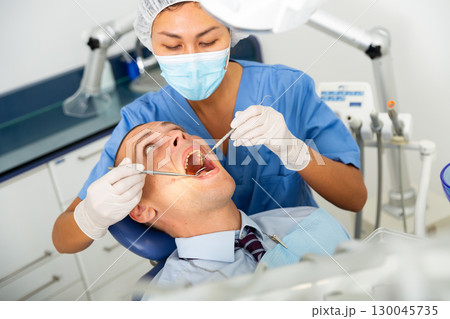 Dentist inspects male patient teeth 130045735