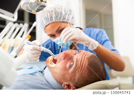 Female dentist drilling tooth to male patient Female dentist drilling tooth to male patient 130045741