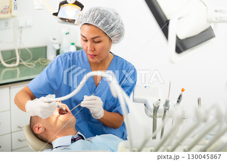 Female dentist drilling tooth to male patient Female dentist drilling tooth to male patient 130045867