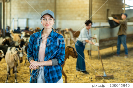 Portrait of young European female farmer in plaid shirt standing with tool while working on goat farm 130045940