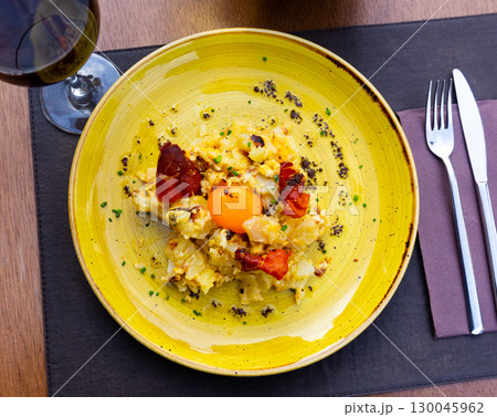 Scramble eggs with potatoes and jamon. Top with raw egg yolk 130045962