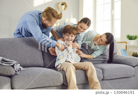 Happy laughing kids boy and girl having fun with their parents, sitting on sofa at home. 130046191