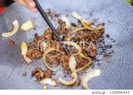 Closeup view of people with chopsticks cooking sliced marinated beef bulgogi on a round grill pan with onions. The scene of the lifestyle of enjoying food in a natural setting 130046445