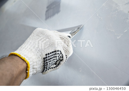 Construction worker in gloves using a scraper to scrape and remove all loose paint on the wall during home renovation. Home renovation project 130046450