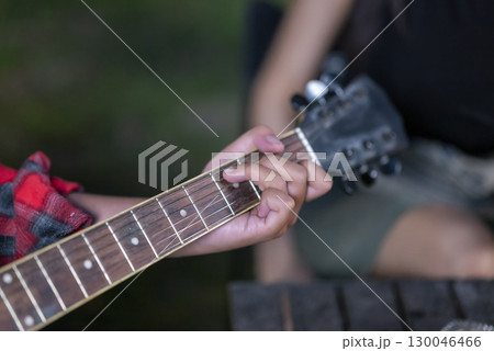 Man playing an acoustic guitar outdoors. Showing a relaxed and enjoyable lifestyle. The scene of the lifestyle of enjoying camping in a natural setting 130046466