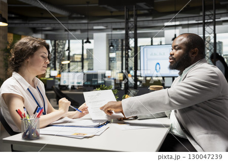 HR manager and job seeker discuss personal and professional benefits package such as salary, rights and other onboarding terms. Reviewing CV and contract document in a corporate setting. 130047239