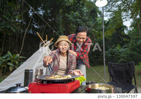 Indonesian southeast asian couple with tongs cooking sliced marinated beef bulgogi on a round grill pan with onions. The scene of the lifestyle of enjoying food in a natural setting Indonesian southeast asian couple with tongs cooking sliced marinated beef bulgogi on a round grill pan with onions. The scene of the lifestyle of enjoying food in a natural setting 130047397