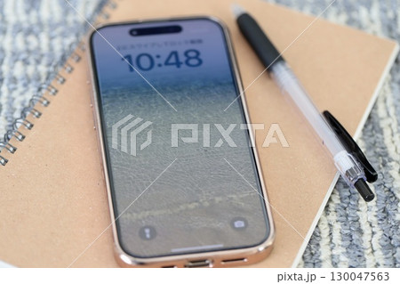 カーペットの上に置いたスマホと筆記用具 130047563