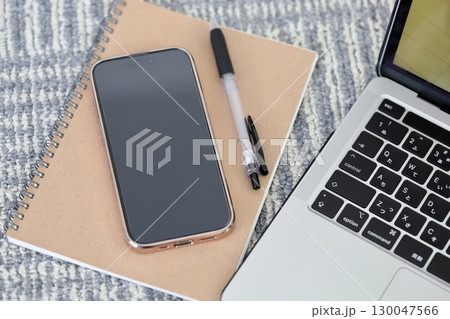 カーペットの上に置いたノートパソコンとスマホと筆記用具 130047566