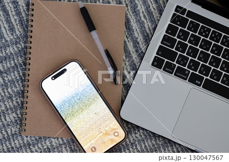 カーペットの上に置いたノートパソコンとスマホと筆記用具 130047567