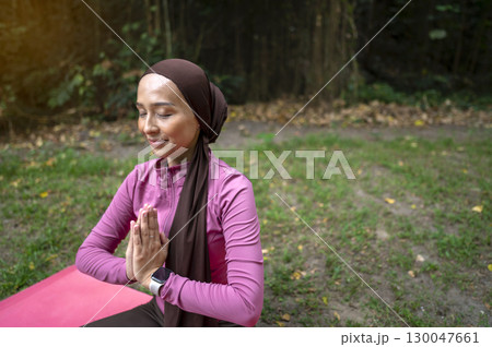 Indonesian southeast asian muslim woman in a sporty outfit relaxing and meditating zen-like in a public park outdoors. Concept of a Healthy active lifestyle Indonesian southeast asian muslim woman in a sporty outfit relaxing and meditating zen-like in a public park outdoors. Concept of a Healthy active lifestyle 130047661