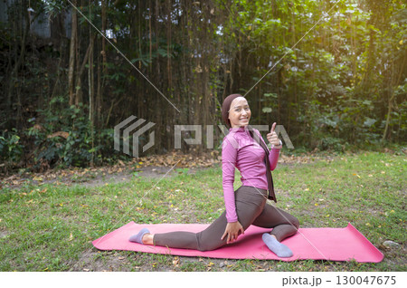 Indonesian southeast asian muslim woman in a sporty outfit practices yoga on a fitness mat in a public park outdoors. Concept of a Healthy active lifestyle Indonesian southeast asian muslim woman in a sporty outfit practices yoga on a fitness mat in a public park outdoors. Concept of a Healthy active lifestyle 130047675