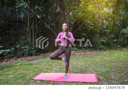 Indonesian southeast asian muslim woman in a sporty outfit practices yoga on a fitness mat in a public park outdoors. Concept of a Healthy active lifestyle Indonesian southeast asian muslim woman in a sporty outfit practices yoga on a fitness mat in a public park outdoors. Concept of a Healthy active lifestyle 130047679