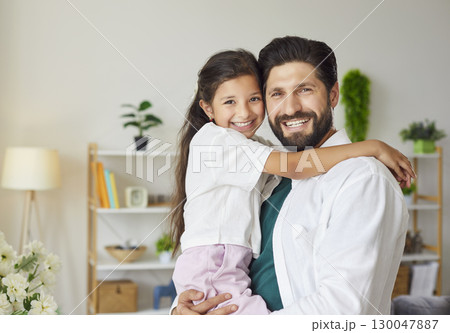 Portrait of smiling bearded father holding his little daughter in modern living room Portrait of smiling bearded father holding his little daughter in modern living room 130047887