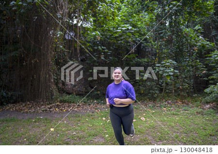 Indonesian southeast asian overweight woman in a sporty outfit practices running exercise in a public park outdoors. Concept of a Healthy active lifestyle and body inclusivity Indonesian southeast asian overweight woman in a sporty outfit practices running exercise in a public park outdoors. Concept of a Healthy active lifestyle and body inclusivity 130048418