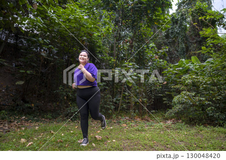 Indonesian southeast asian overweight woman in a sporty outfit practices running exercise in a public park outdoors. Concept of a Healthy active lifestyle and body inclusivity Indonesian southeast asian overweight woman in a sporty outfit practices running exercise in a public park outdoors. Concept of a Healthy active lifestyle and body inclusivity 130048420